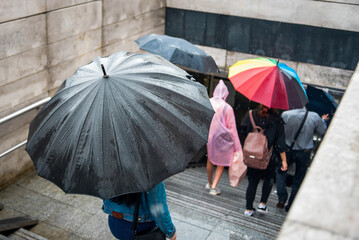 People with umbrellas descend into the underpass. Cityscape on a rainy day. Umbrella with raindrops. Bad weather. City street style.