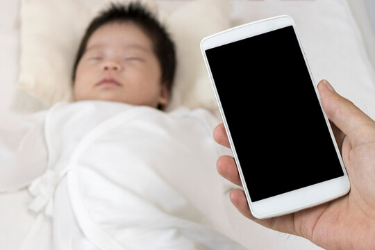 スマートフォンを操作する男の手と、眠っている赤ちゃん