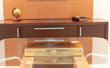 Caixa dourada em cima de uma mesa de vidro em um escritório clean moderno de madeira