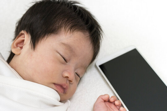 眠っている赤ちゃんとノートパソコン。デジタルネイティブ世代のイメージ