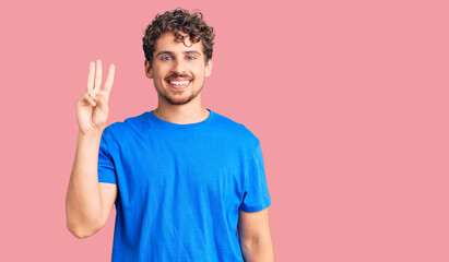Young handsome man with curly hair wearing casual clothes showing and pointing up with fingers number three while smiling confident and happy.