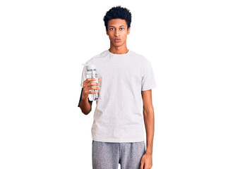 Young african american man wearing sportswear holding water bottle thinking attitude and sober expression looking self confident
