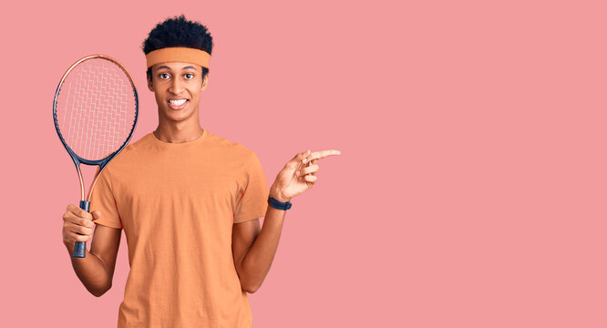 Young african american man playing tennis holding racket smiling happy pointing with hand and finger to the side