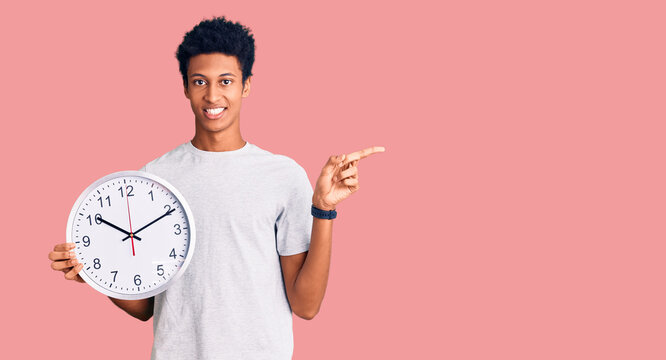 Young african american man holding big clock smiling happy pointing with hand and finger to the side