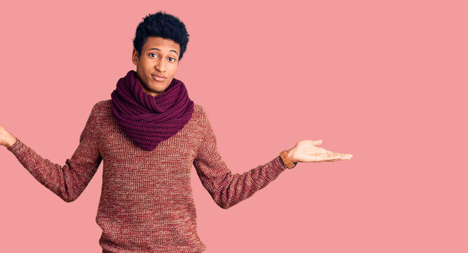 Young african american man wearing casual winter sweater and scarf clueless and confused expression with arms and hands raised. doubt concept.