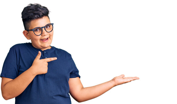 Little boy kid wearing casual clothes and glasses amazed and smiling to the camera while presenting with hand and pointing with finger.