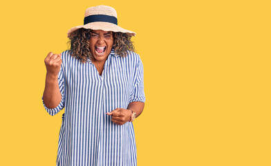 Young african american plus size woman wearing summer hat angry and mad raising fist frustrated and furious while shouting with anger. rage and aggressive concept.