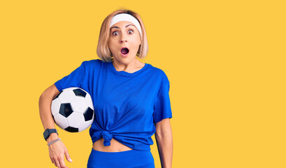 Young blonde woman holding soccer ball scared and amazed with open mouth for surprise, disbelief face