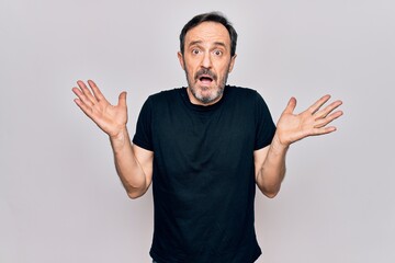 Fototapeta premium Middle age man wearing casual black t-shirt standing over isolated white background clueless and confused with open arms, no idea and doubtful face.