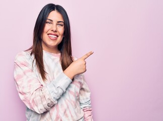 Young beautiful brunette woman wearing casual dyed sweatshirt over isolated pink background smiling cheerful pointing with hand and finger up to the side