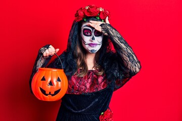 Young woman wearing day of the dead costume holding pumpkin stressed and frustrated with hand on head, surprised and angry face
