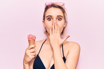 Young beautiful blonde woman wearing bikini holding ice cream covering mouth with hand, shocked and afraid for mistake. surprised expression