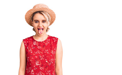 Young beautiful blonde woman wearing summer hat sticking tongue out happy with funny expression. emotion concept.