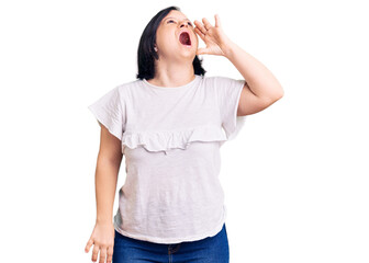 Fototapeta premium Brunette woman with down syndrome wearing casual white tshirt shouting and screaming loud to side with hand on mouth. communication concept.