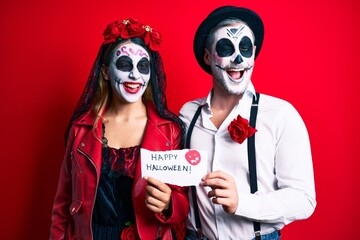 Couple wearing day of the dead costume holding happy halloween paper winking looking at the camera with sexy expression, cheerful and happy face.