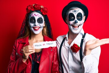 Couple wearing day of the dead costume holding trick or treat paper celebrating victory with happy smile and winner expression with raised hands