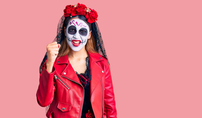 Woman wearing day of the dead costume over background angry and mad raising fist frustrated and furious while shouting with anger. rage and aggressive concept.
