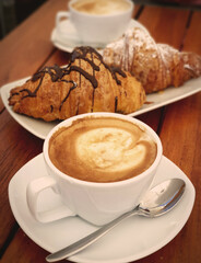 The cup of cappuccino with chocolate croissants in the background - traditional italian breakfast