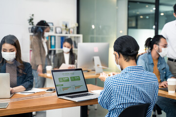 Asian young business man washing hand before working on computer in office with new normal lifestyle concept. Man and woman wear protective face mask and keep social distancing to prevent covid virus.