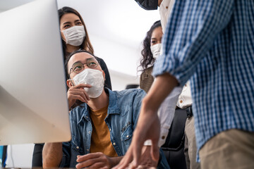 Asian young business people wearing mask working on computer in office
