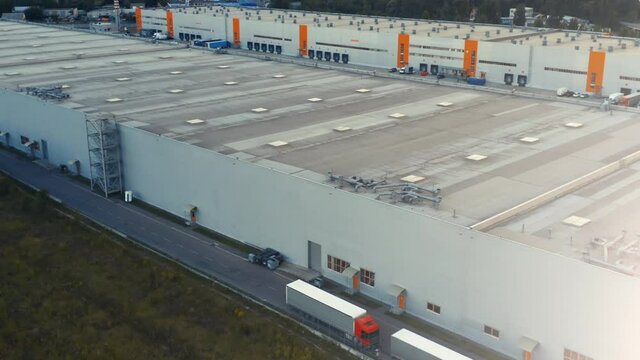 Aerial view of a big logistics park, loading hub. Semi trucks with cargo trailers standing along the warehouse and waiting for loading/unloading goods
