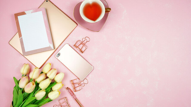 Feminine pink theme desktop workspace with rose gold tablet and phone devices on stylish textured background. Top view blog hero header creative composition flat lay.