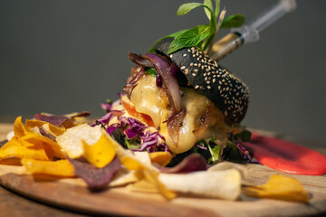 Tasty Black burger with meat patty, cheese, tomatoes, mayonnaise, purple and orange sweet potato, taro Crisps. Wooden cutting board isolated on Dark Slate Gray Concrete Wall background