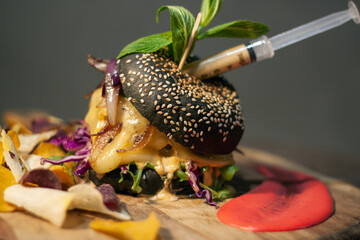 Tasty Black burger with meat patty, cheese, tomatoes, mayonnaise, purple and orange sweet potato, taro Crisps. Wooden cutting board isolated on Dark Slate Gray Concrete Wall background