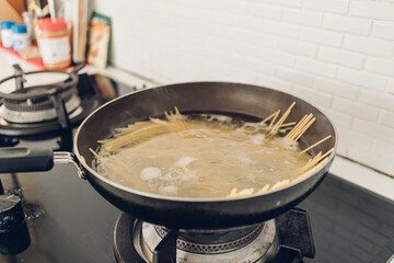 Image of boiling spaghetti with the pan in white kitchen.