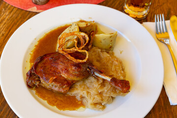 Delicious crispy braised duck leg served with sauerkraut, potato dumplings and onion rings