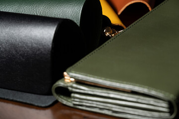 4 colors leather sample(black,green,yellow,brown) on wooden table with green wallet with gold-colored metal clasp.Materials for leather industry.