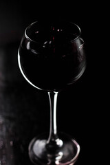 Large silhouette of a glass on a black background, with a red drink inside. A drop falls from above