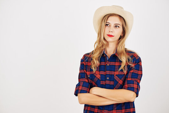 Pensive young woman in plaid shirt and hat crossing arms and looking away