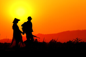 Silhouette of a soldier meeting in love with a Vietnamese woman in the sunset.