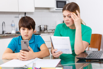 Frustrated boy using smartphone while mother berating him