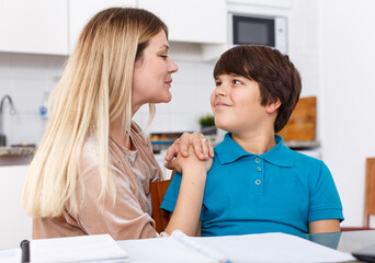 Portrait of smiling mother helping son with homework and having good time in kitchen
