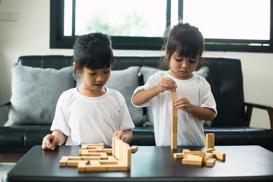 Two happy siblings playing a game with wooden blocks at home joyfully