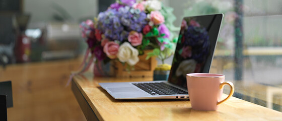 Portable workspace with laptop, coffee mug and flower vase on counter bar in cafe
