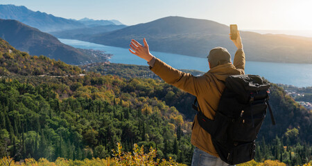 Traveler with a backpack and a smartphone stands on a mountain