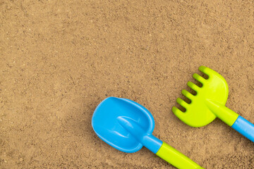 Fototapeta na wymiar Shovel and rake in sandbox. Outdoor children's sand toys. Summer concept. With place for text.