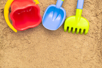 Fototapeta na wymiar Children's sand toys: shovel, rake and bucket. Sandbox outdoor. Summer concept. With place for text.