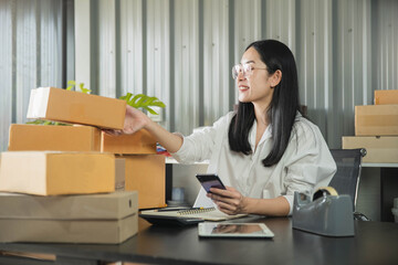 Fototapeta na wymiar Young business woman working online e-commerce shopping at her shop. Young woman seller prepare parcel box of product for deliver to customer. Online selling, e-commerce.