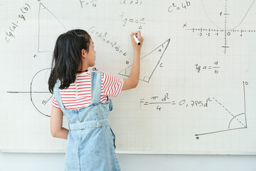 Smart schoolgirl writing on whiteboard when solving geometry task in class, view from the back