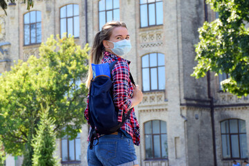 Young woman in protective mask is standing outdoors near university. Back to school after quarantine. New normal.