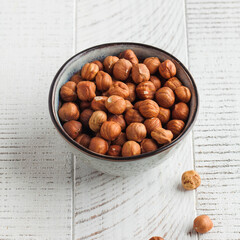 A handful of hazelnuts in a grey bowl on a white wooden background. Healthy snacks. Nuts.