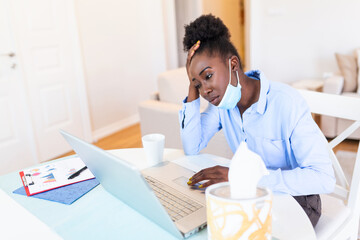 Woman sitting alone in her office and coughing as she suffers from a cold. Medical mask and hand disinfectant and stressed woman. Shot of a businesswoman working in her office while shi is sick.