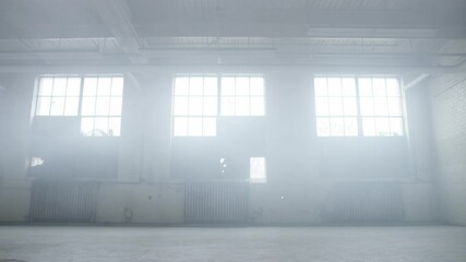 Contemporary dancer dances in industrial warehouse with lots of energy and passion surrounded by mist, smoke and soft light