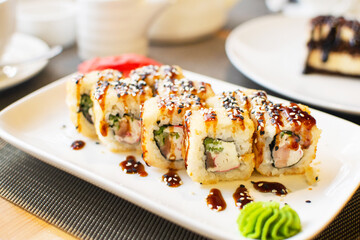 Delicious hot rolls with salmon, cream cheese Philadelphia, cucumber and eel on white plate. Japanese food in restaurant. Selective focus.