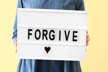 Woman holding board with word FORGIVE on color background, closeup