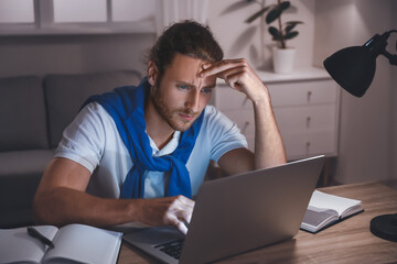 Tired male student using laptop for online learning at home